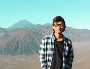 Portrait of young man standing on mountain against clear sky