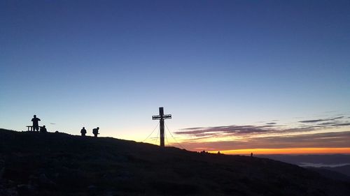 Silhouette cross on land against clear sky during sunset