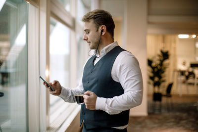 Businessman wearing headphones using mobile phone while having coffee at office