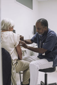 Mature male doctor examining senior female patient in medical clinic