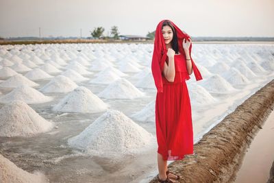 A beautiful woman in a long red dress stands tall among salt fields and blue skies.