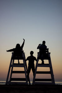 People sitting on lifeguard chairs against sea during sunset