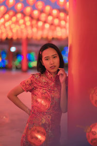 Portrait of young woman standing against illuminated wall