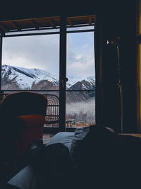 Low section of man sitting on bed by window against snowcapped mountains