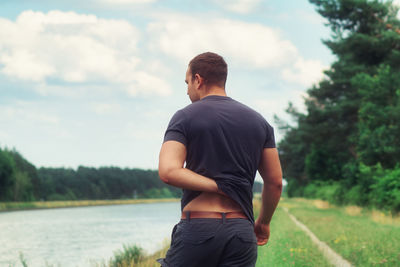 Rear view of man scratching back while standing at lakeshore