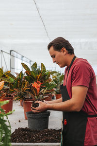 Side view of young man standing by potted plants