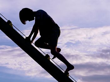 Silhouette boy climbing ladder against sky