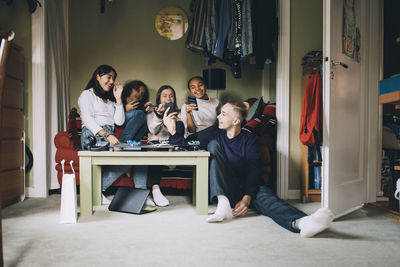 Cheerful friends talking while looking at smart phone in living room