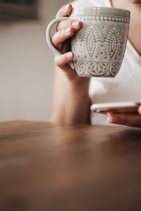 Midsection of woman holding coffee cup on table