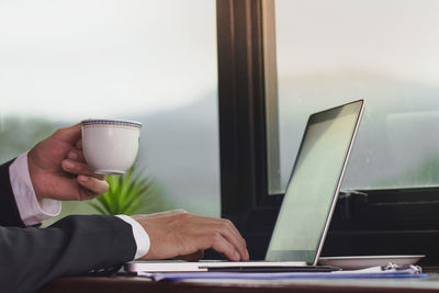 Young businessman holding mug of coffee while working on laptop computer