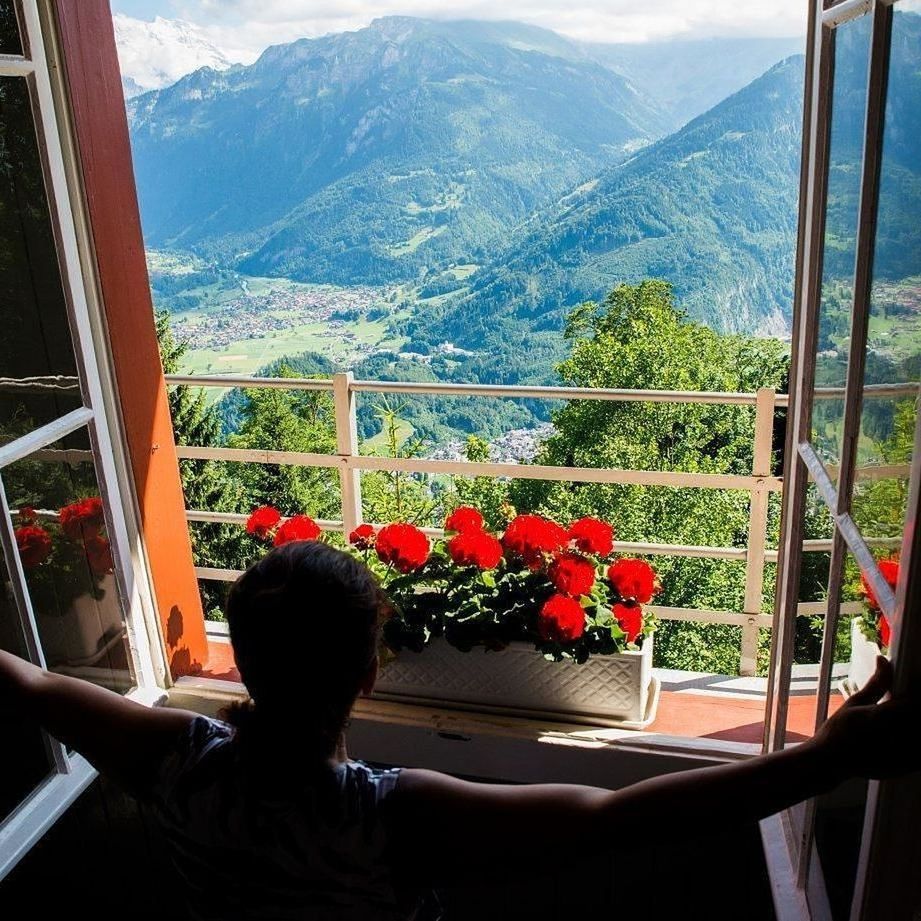 REAR VIEW OF WOMAN LOOKING THROUGH WINDOW IN BALCONY