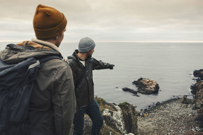 Man pointing at rock in sea to male friend during vacation