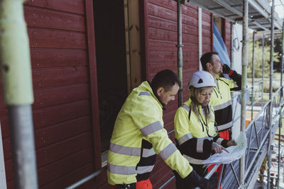 Female builder discussing over floor plan with male colleague at scaffolding