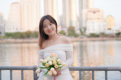 Portrait of young woman standing against river