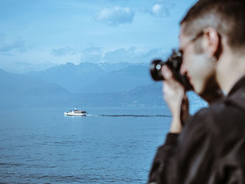 Side view of man photographing sea against blue sky