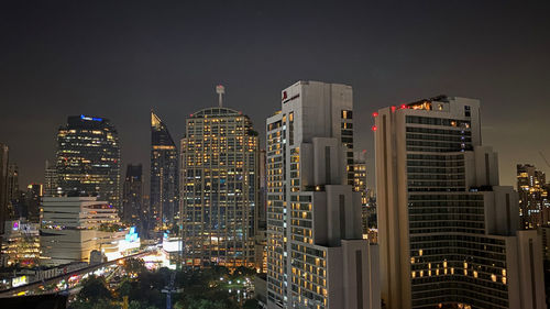 Illuminated modern buildings in city against sky at night