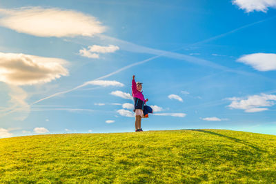 Low angle view of child standing on grassy hill against cloudy sky during sunny day
