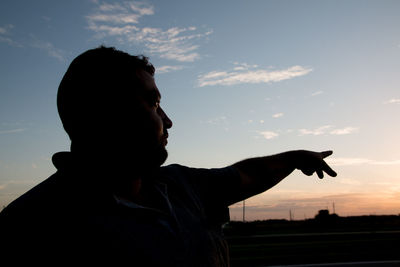 Man pointing against sky during sunset