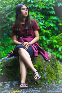 Young woman looking away while sitting on tree