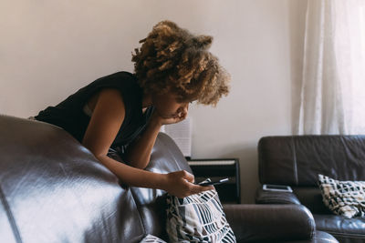 Girl using smart phone leaning on sofa at home