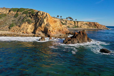 Rock formations on shore against clear blue sky