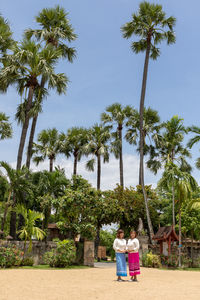 Rear view of women standing by palm trees against sky