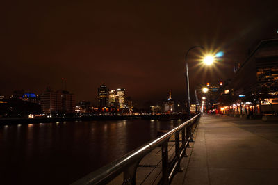 Illuminated buildings by river against sky at night