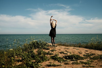 Blonde girl from the back in a black dress on a cliff over the sea. high quality photo