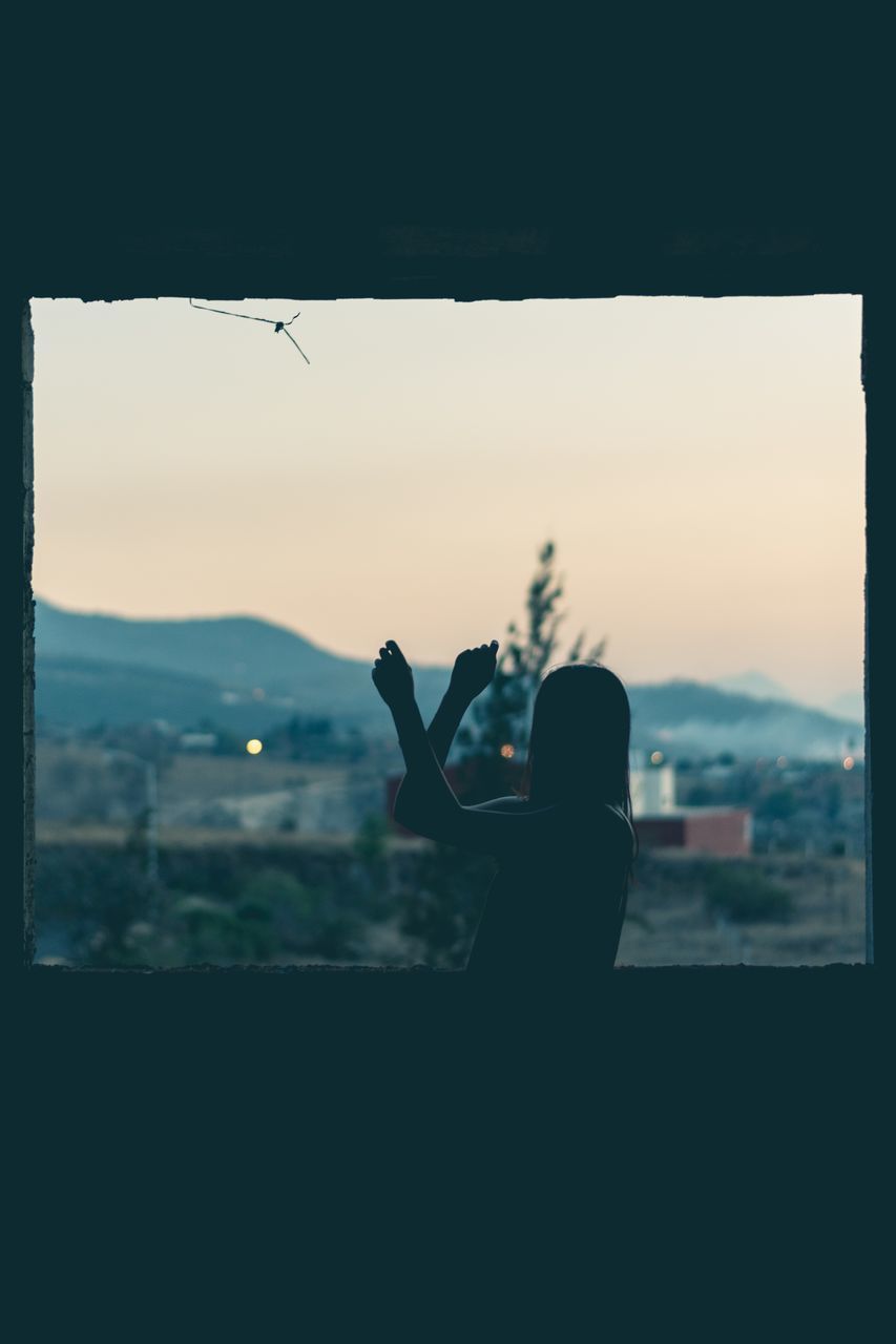 SILHOUETTE OF WOMAN PHOTOGRAPHING THROUGH WINDOW