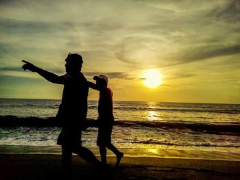 Silhouette couple standing at beach during sunset