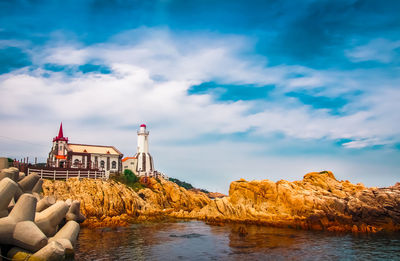 Lighthouse amidst sea and buildings against sky