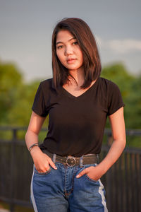 Portrait of young woman standing against trees