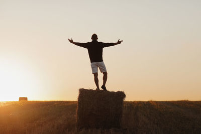 Rear view of man standing on field against sky during sunset