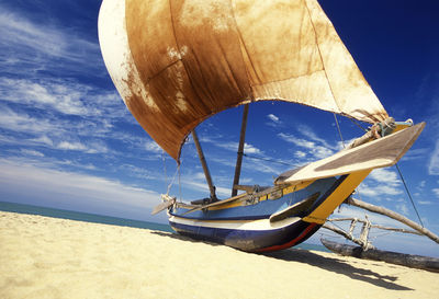 Outrigger boat moored at beach during sunny day