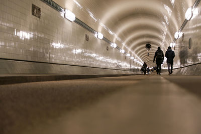 Rear view of people walking in illuminated tunnel