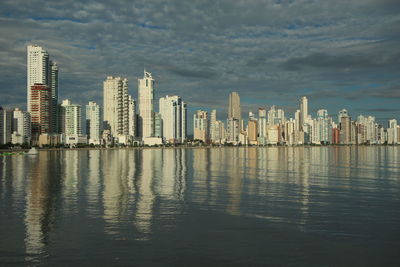 View of city at waterfront against cloudy sky