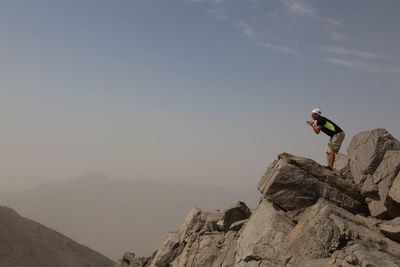 Side view of man standing on rock against sky