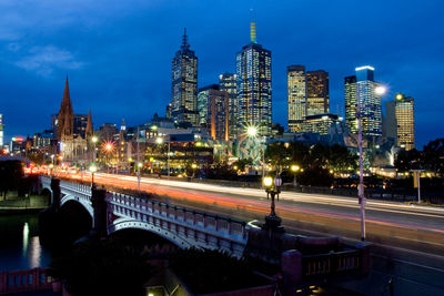 Light trails on street amidst buildings against sky at night