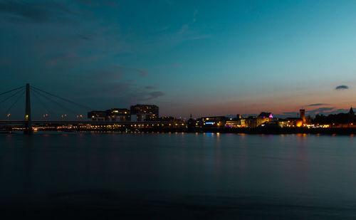 Illuminated city by river against sky at night