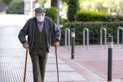 Senior man wearing protective face mask walking on footpath during covid-19