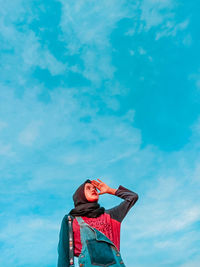 Low angle view of young woman standing against blue sky