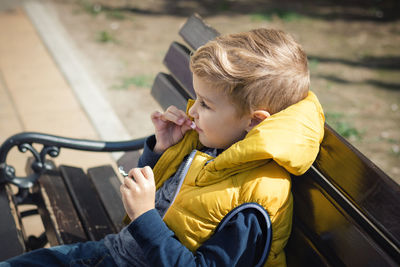 Cute boy eating jellybean while sitting on bench in park