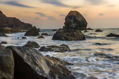 Rocks in sea against sky during sunset