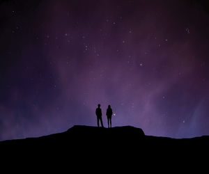 Low angle view of silhouette man and woman standing on cliff against star field