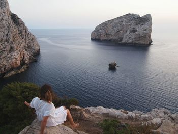 Rear view of people sitting on rock by sea