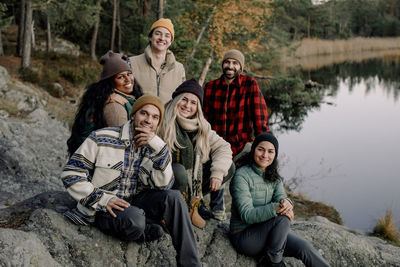 Portrait of smiling multiracial male and female friends sitting on rock during staycation