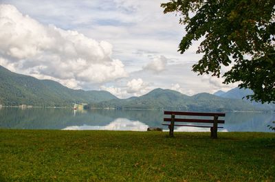 Bench in park by lake against sky