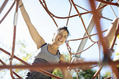 Healthy happy woman hanging on rope web in park