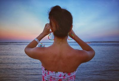 Sunburnt back of a woman on a beach looking a colorful rainbow colorful sunset blue sea water dress