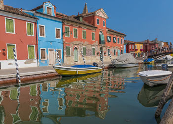 Boats moored in canal by buildings against sky